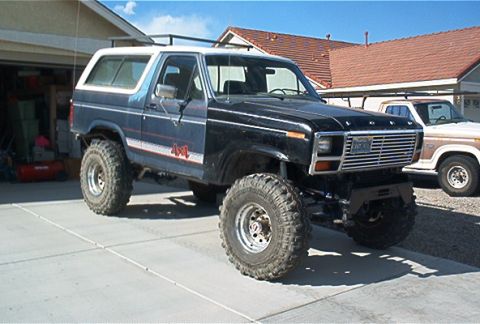 1986 Ford Bronco - A modified Ford Bronco with a custom grille and off-road tires sits in a driveway next to another truck.