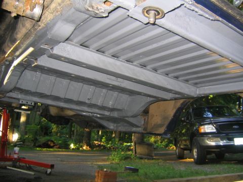 1978 Ford Bronco - Underside view of a body tub lifted off its frame and freshly coated in gray primer/paint, showing ribbed floor pans, rocker rails and a bo…