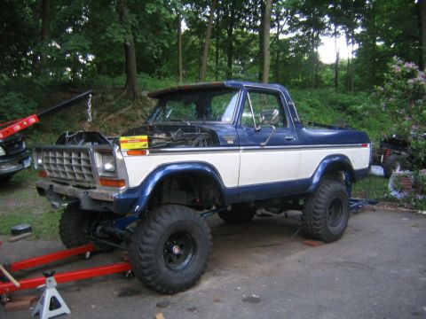 1978 Ford Bronco - Driver-side view of a two-tone blue-over-white full-size Ford Bronco, lifted on large mud-terrain tires with black wheels and a chrome eggc…