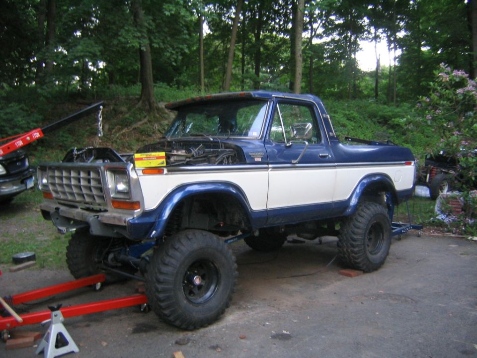 Two-tone blue and white lifted full-size Ford Bronco, driver side, on jack stands