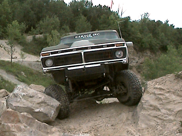 1977 Ford F-150 climbing over rocks on a dirt trail, with 'DAMAGE INC' sticker on windshield