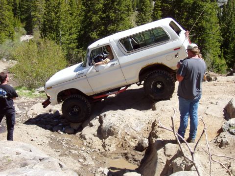1979 Ford Bronco - White Ford Bronco tackling a challenging off-road obstacle on a sunny day.