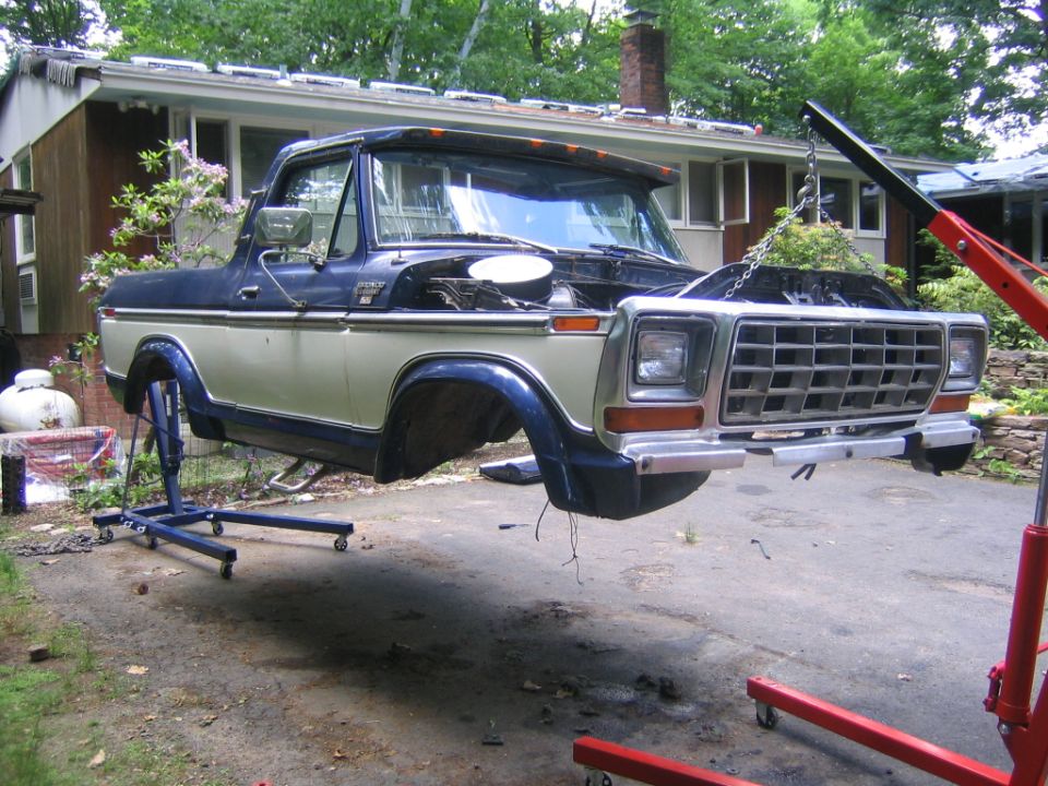 Two-tone Ford Bronco with top and doors removed, front end on an engine hoist