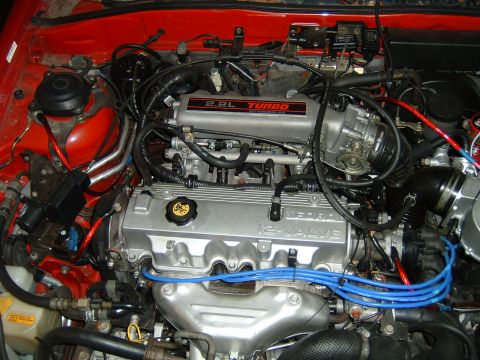 1989 Ford Probe - The engine bay of a vehicle is shown, a 2.2L turbo 12-valve engine with prominent blue spark plug wires.