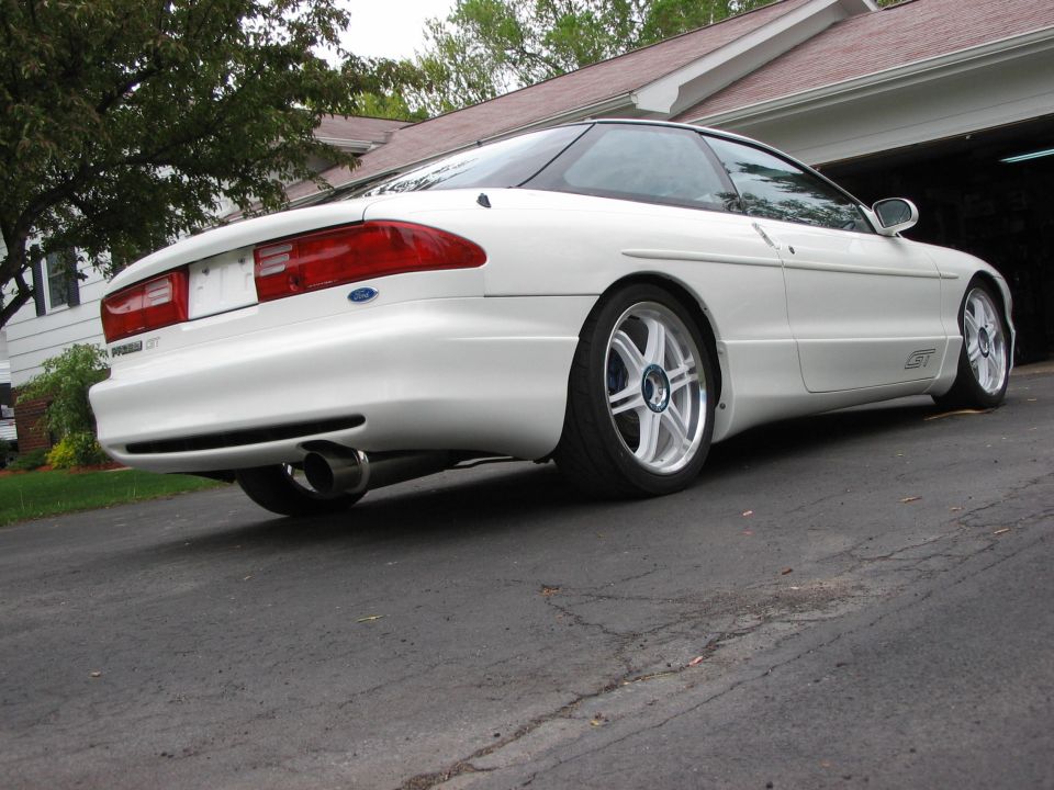 White Ford Probe GT parked in driveway, rear quarter view. Aftermarket exhaust and wheels