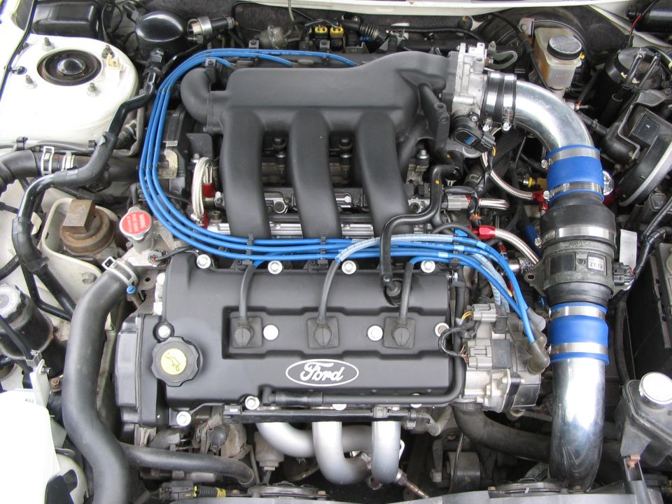 Close-up of a Ford engine with blue spark plug wires and silver intake piping