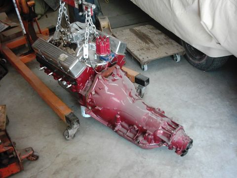 1978 Ford Bronco - Engine and transmission assembly suspended by a hoist in a garage setting.