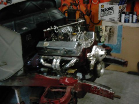 1978 Ford Bronco - Engine assembly with chrome headers and intake manifold is displayed on a red stand in a workshop.