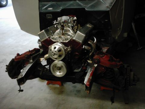 1978 Ford Bronco - Engine and front suspension assembly, likely undergoing restoration or repair, is displayed on red support stands.
