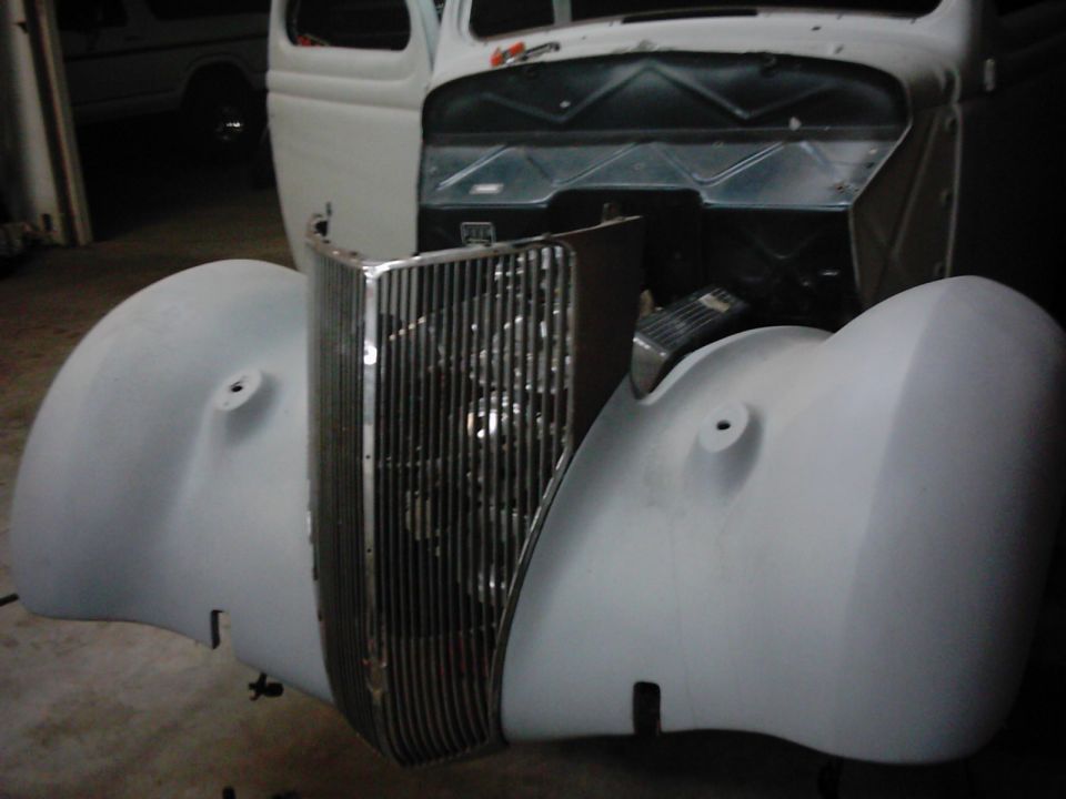 Gray primer fenders and vertical bar grille of a vintage car under repair
