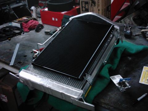 1978 Ford Bronco - A radiator is shown on a workbench, surrounded by various tools and automotive parts, suggesting a repair or upgrade process.