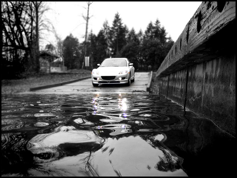 Silver Mazda RX-8 front view reflected in a puddle on a wet driveway, black-and-white scene