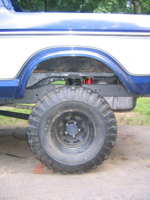 1978 Ford Bronco - Rear wheel well of a blue and white Ford Bronco showing a large mud-terrain tire labeled 'Gumbo Monster Mudder' on a black steel wheel, wit…