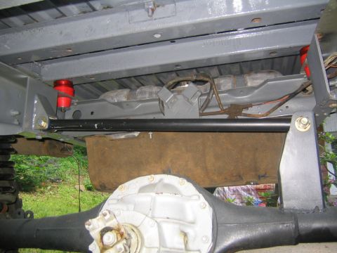 1978 Ford Bronco - Underbody view looking up at a truck's rear frame and axle, with a black rear track bar/anti-sway bar spanning between frame brackets, red…
