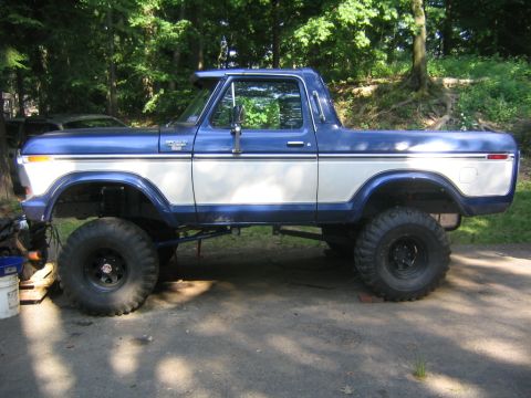 1978 Ford Bronco - A two-tone blue and white 1978 Ford Bronco shown in side profile, lifted with oversized off-road mud tires on black steel wheels. The remov…