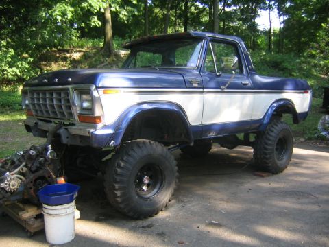 1978 Ford Bronco - A blue and white 1978 Ford Bronco with a lift kit and large mud-terrain tires on black wheels, shown from the front-left three-quarter angl…