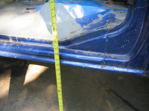 1978 Ford Bronco - Close-up of a blue truck's lower door and rocker panel showing bare body filler and gray primer over a repair, with a yellow tape measure h…
