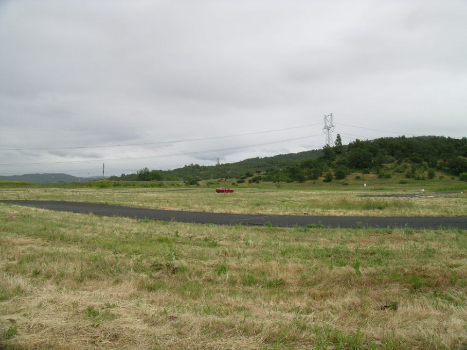 Red coupe on a grassy field with a paved track in foreground and hills in background