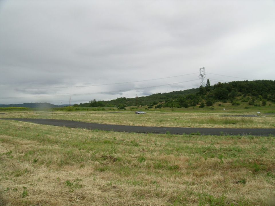 Silver sedan driving on a paved track in a grassy field under a cloudy sky