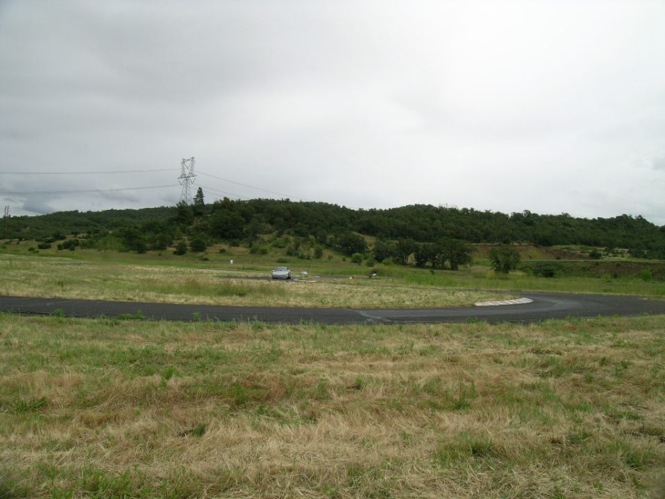 Silver car parked on grassy field next to a race track