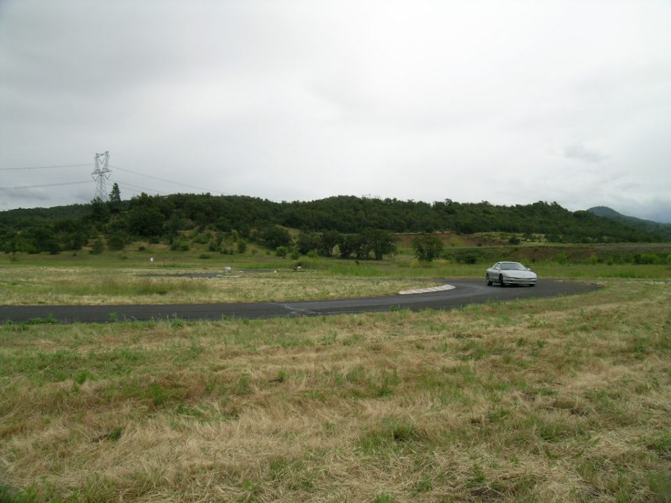 Silver coupe driving on a race track with grassy fields and trees in the background