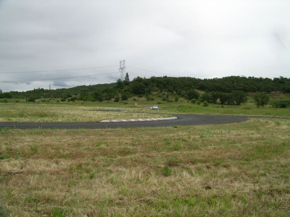 Silver car on a race track with rolling hills and power lines in the background