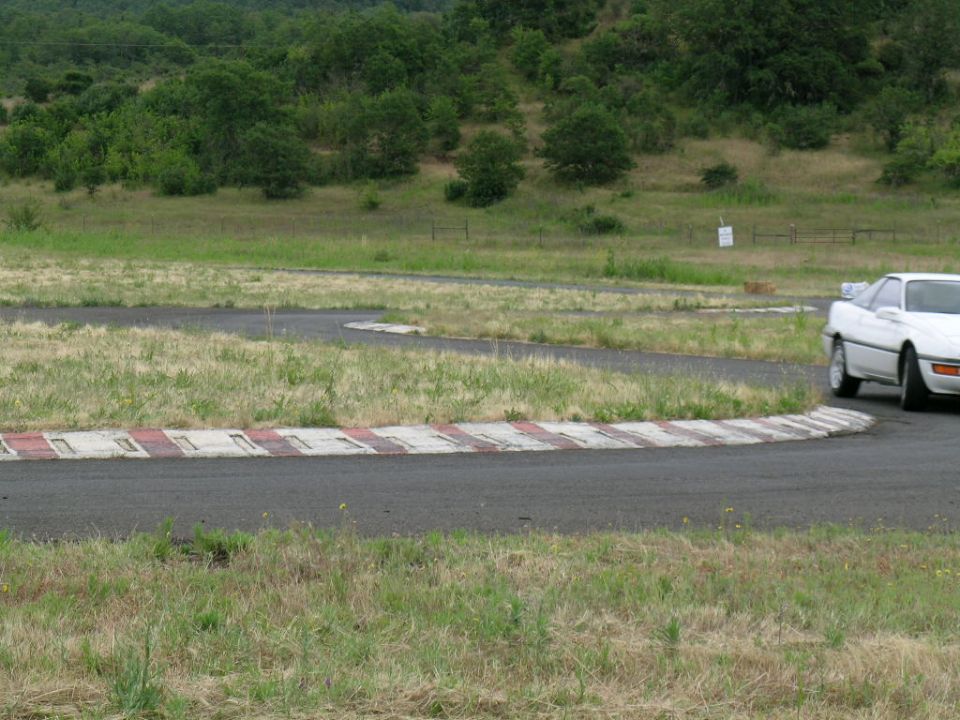 White sports coupe rounding a tight red-and-white curbed corner on a road course