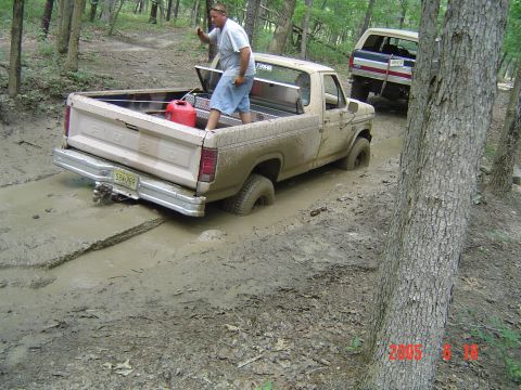 1986 Ford F-250 - A man stands in the bed of a muddy Ford pickup truck that is stuck in a muddy trail, with another vehicle behind it.