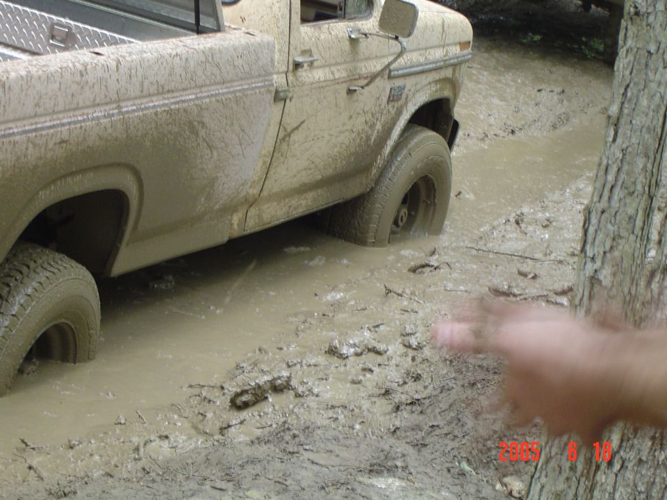 Mud-covered pickup truck stuck in mud, side view. The front wheel is submerged
