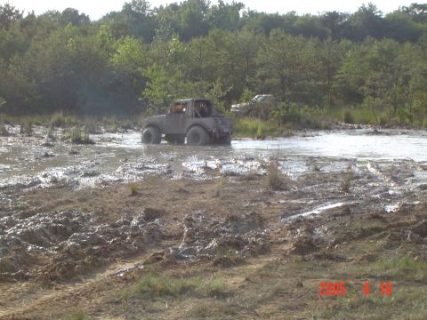 1986 Ford F-250 - An off-road vehicle navigates through a muddy terrain, with another vehicle partially visible in the distance.