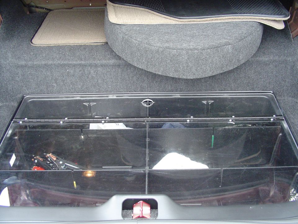 Trunk of a sedan with clear plastic storage organizer holding jack and tools, gray carpeted spare tire cover behind