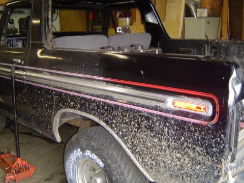 1979 Ford Bronco - Passenger-side profile of a topless black Ford Bronco inside a garage, its bodywork and dust-flecked paint showing the chrome bodyside mold…