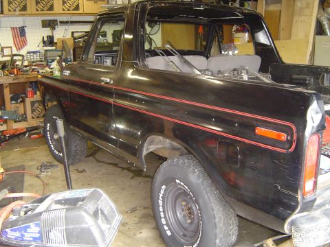 1979 Ford Bronco - Rear three-quarter view of a black square-body Ford Bronco with red pinstripe body-side tape and the removable hardtop off, exposing the ro…