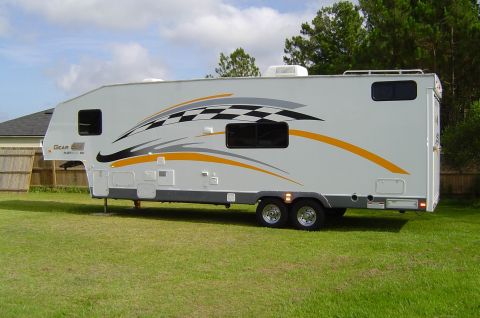 1993 Ford Bronco - A white fifth wheel RV is parked on a grassy lawn, racing-inspired graphics along its side.