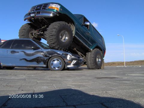 1996 Ford Bronco - A lifted green Ford Bronco is parked on top of a silver car with flame graphics.