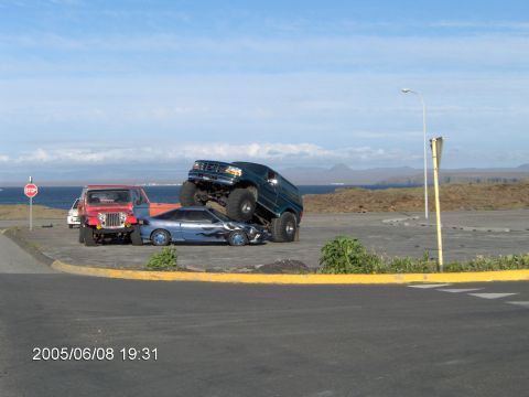 1996 Ford Bronco - A lifted 1996 Ford Bronco is parked on top of a blue sports car near a body of water.