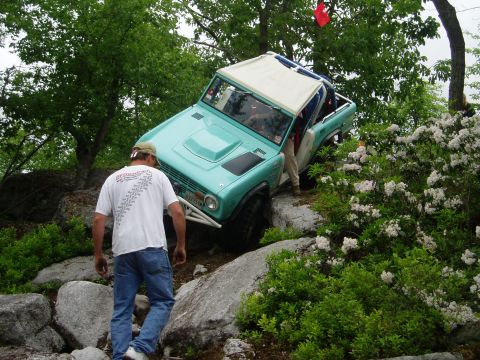1969 Ford Bronco - Teal Ford Bronco with white roof and roll cage is shown off-roading on a rocky trail.