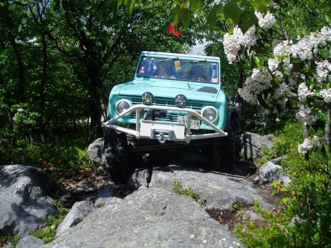1969 Ford Bronco - A teal 1969 Ford Bronco navigates a challenging rocky terrain, equipped with a winch and off-road lights.