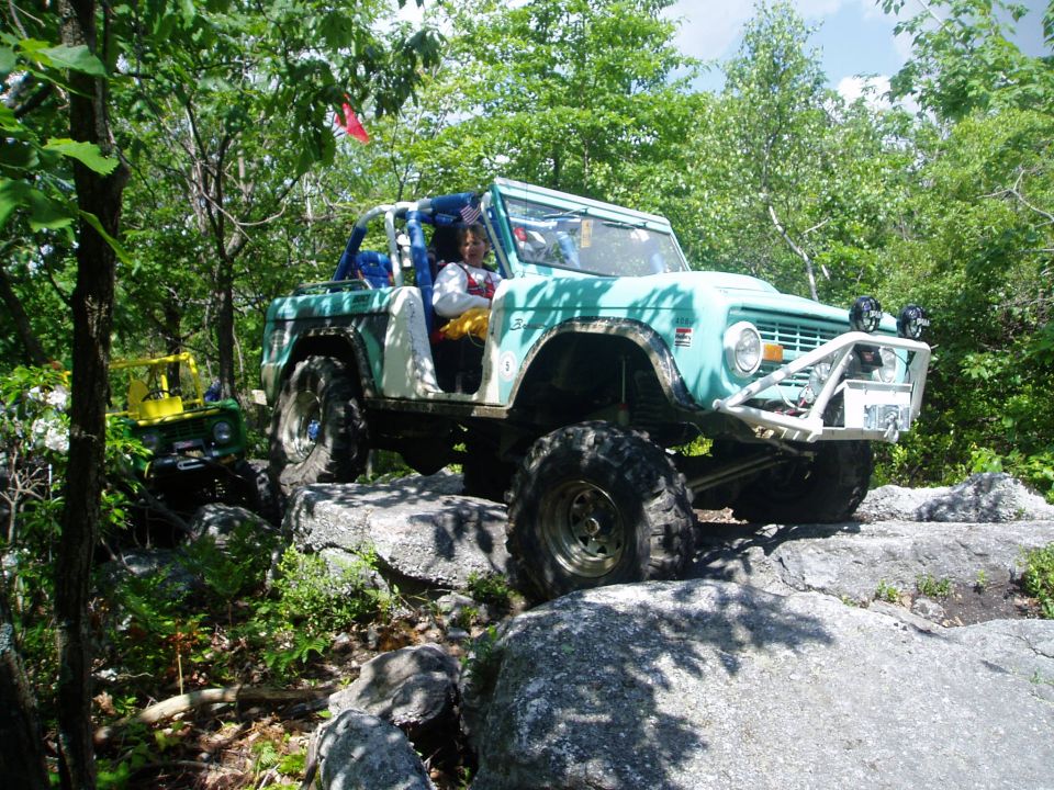 light blue off-road vehicle with large tires navigating rocky terrain, another yellow vehicle behind it