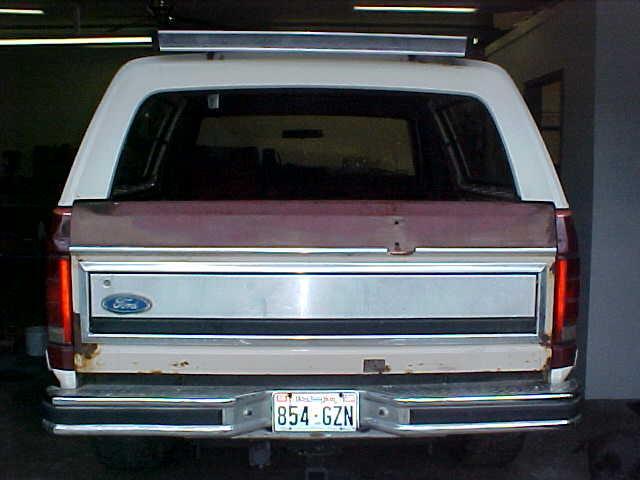 Rear of white-and-maroon Ford Bronco with rusty tailgate and Washington plate 854-GZN