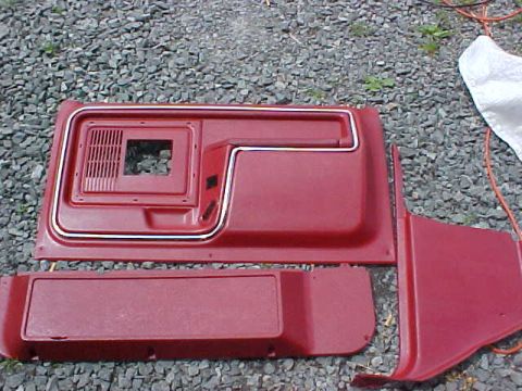 1983 Ford Bronco - Red interior door panels and trim pieces are laid out on a gravel surface, possibly for restoration or sale.