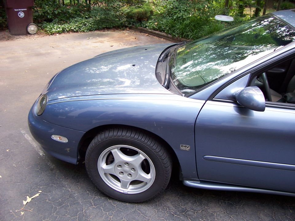 Blue sedan front fender and wheel, parked on cracked asphalt