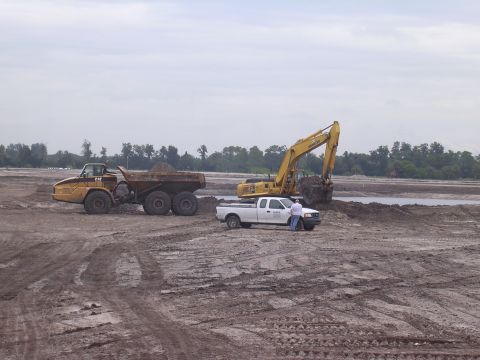 1985 Ford Bronco - A white pickup truck is parked near an excavator and a dump truck at a muddy construction site.