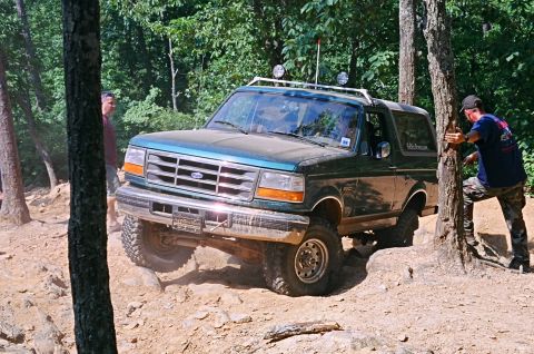 1990 Ford Bronco - A green Ford Bronco navigates a challenging off-road course, with two individuals observing the action.