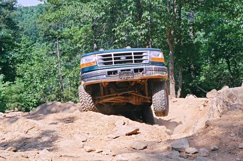 1990 Ford Bronco - This Ford truck navigates a rocky off-road path with its front wheels elevated.