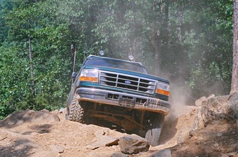 1990 Ford Bronco - This SUV is shown tackling a challenging off-road course with dust and debris kicked up.