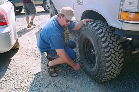 1990 Ford Bronco - A man kneels to check the tire pressure on a large off-road vehicle, with other vehicles visible in the background.
