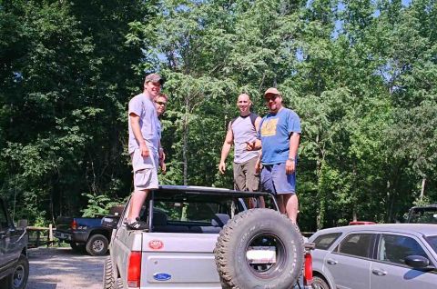 1990 Ford Bronco - Four men stand on and around a silver Ford Bronco, with a spare tire mounted on the back, in a wooded area.