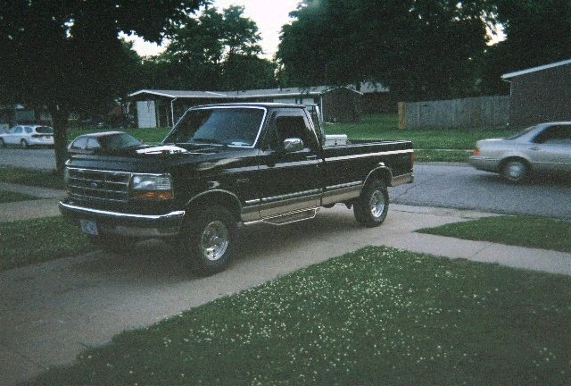 Black Ford F-150 with chrome wheels parked in a suburban driveway at dusk