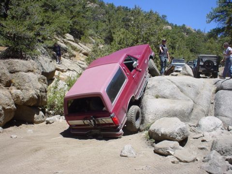 1991 Ford Bronco - A red 1991 Ford Bronco is shown attempting to climb over large rocks on an off-road trail.